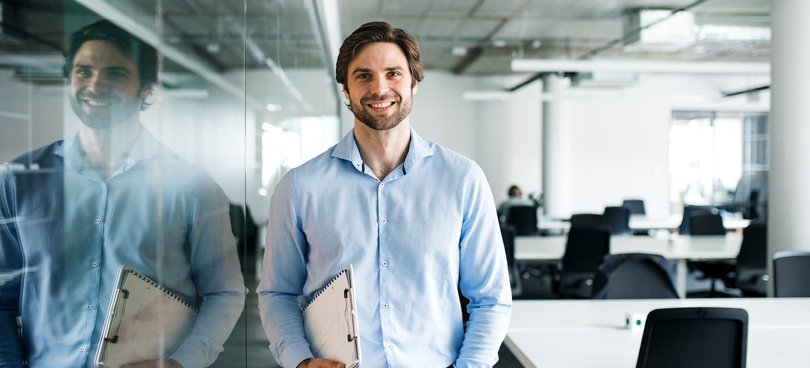 Profissional a segurar um caderno num escritório moderno, junto a uma parede de vidro.