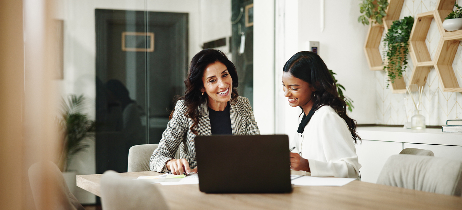 Duas profissionais reunidas numa sala de reuniões, a trabalhar em documentos com um portátil aberto sobre a mesa.